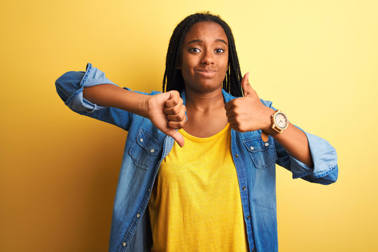 Young african american woman wearing denim shirt standing over isolated yellow background Doing thumbs up and down, disagreement and agreement expression. Crazy conflict