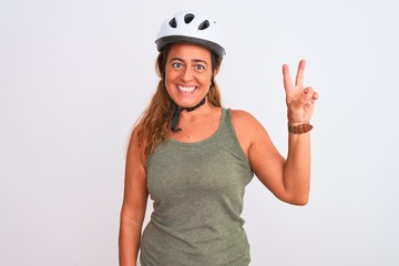 Middle age mature cyclist woman wearing safety helmet over isolated background showing and pointing up with fingers number two while smiling confident and happy.