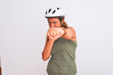 Middle age mature cyclist woman wearing safety helmet over isolated background Punching fist to fight, aggressive and angry attack, threat and violence
