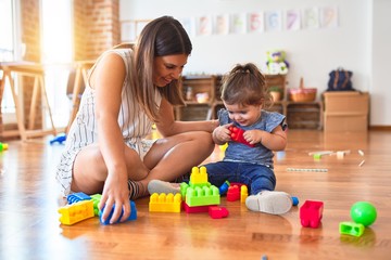 Young beautiful teacher and toddler playing with building blocks toy at kindergarten