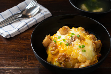 Oyakodon or donburi in black bowl with Miso soup on wooden table.