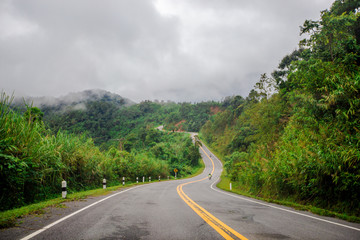 Blurred background of a mountain road view, from a car windscreen that runs with care, with natural scenery surrounded by plants, large trees