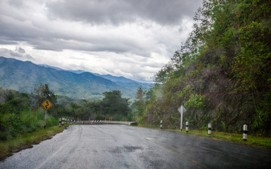 Blurred background of a mountain road view, from a car windscreen that runs with care, with natural scenery surrounded by plants, large trees