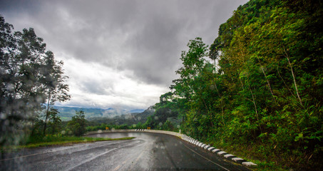 Blurred background of a mountain road view, from a car windscreen that runs with care, with natural scenery surrounded by plants, large trees