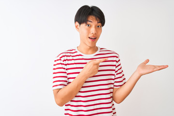 Young chinese man wearing casual striped t-shirt standing over isolated white background amazed and smiling to the camera while presenting with hand and pointing with finger.