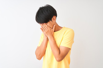 Chinese man wearing yellow casual t-shirt standing over isolated white background with sad expression covering face with hands while crying. Depression concept.
