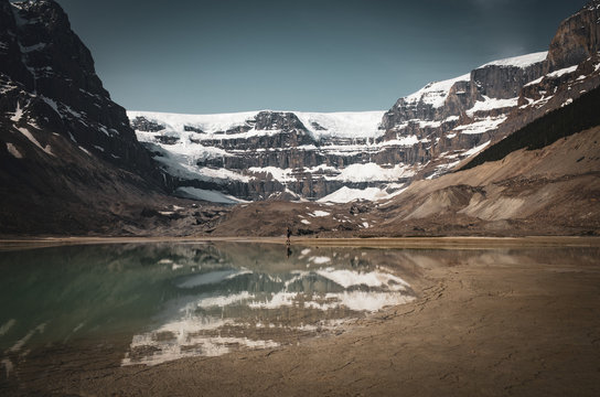 Young adventure man hiking toward the glacier in Jasper National park, Alberta, Canada. View to mountains, glacier and mirror reflection of landscape in the water, moody picture, Icefields Parkway