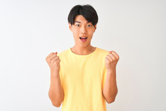 Chinese man wearing yellow casual t-shirt standing over isolated white background celebrating surprised and amazed for success with arms raised and open eyes. Winner concept.