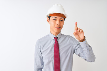 Chinese architect man wearing tie and helmet standing over isolated white background showing and pointing up with finger number one while smiling confident and happy.