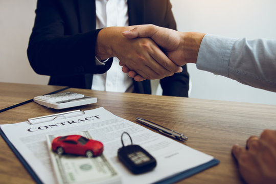 New car buyers and car salesmen are shaking hands to make agreements about car sales.