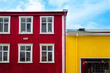 Reykjavik, Iceland - Apr 28 2019: Typical fisherman's colorful houses in Reykjavik with red and yellow metallic facade and white six framed wooden windows. Colorful contrast concept. Blue cloudy sky.