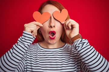 Young redhead romantic woman holding heart over red isolated background scared in shock with a surprise face, afraid and excited with fear expression