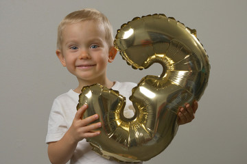 Portrait of cute little boy holds balloon, smiles, looks at camera. Three years old child, birthday