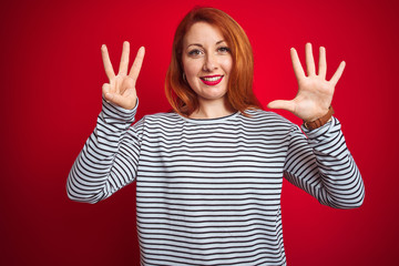 Young redhead woman wearing strapes navy shirt standing over red isolated background showing and pointing up with fingers number eight while smiling confident and happy.