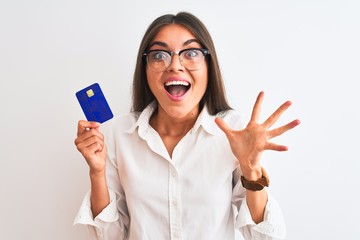 Young businesswoman wearing glasses holding credit card over isolated white background very happy...