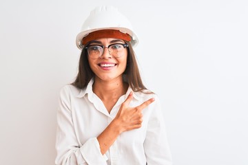 Young beautiful architect woman wearing helmet and glasses over isolated white background cheerful with a smile of face pointing with hand and finger up to the side with happy and natural expression