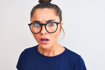 Beautiful woman with bun wearing blue t-shirt and glasses over isolated white background scared in shock with a surprise face, afraid and excited with fear expression