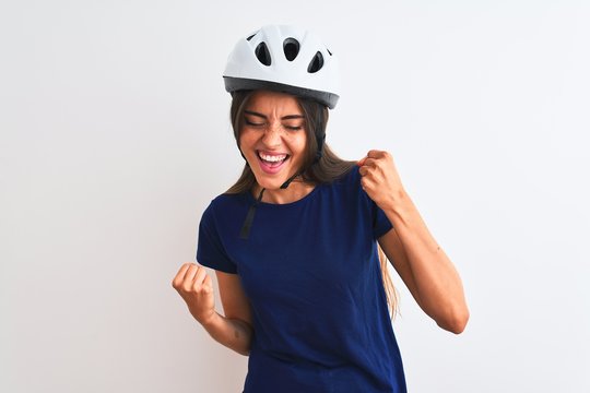 Young beautiful cyclist woman wearing security bike helmet over isolated white background very happy and excited doing winner gesture with arms raised, smiling and screaming for success. 