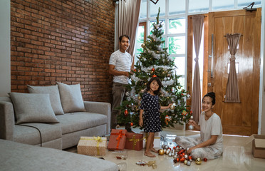 family and daughter hanging some accessories on christmas tree together