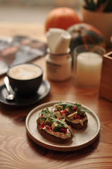 vegetarian food, sandwich with avocado, rucola and sun-dried tomatoes with a cup of coffee on the background, on a wooden table