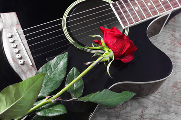 Black acoustic guitar and red rose on a wooden background