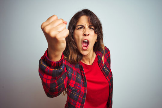 Young beautiful woman wearing red t-shirt and jacket standing over white isolated background angry and mad raising fist frustrated and furious while shouting with anger. Rage and aggressive concept.