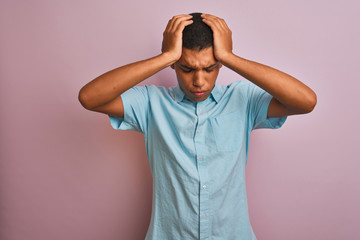 Young handsome arab man wearing blue shirt standing over isolated pink background suffering from headache desperate and stressed because pain and migraine. Hands on head.