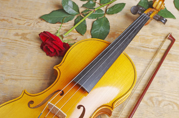 Fototapeta na wymiar Violin with a bow and a red rose on a wooden invoice.