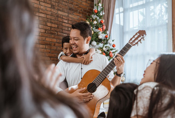 family and friend singing a song together. father playing guitar during christmas