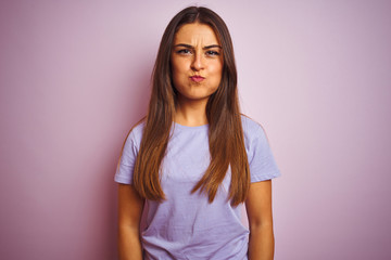 Young beautiful woman wearing casual t-shirt standing over isolated pink background puffing cheeks with funny face. Mouth inflated with air, crazy expression.