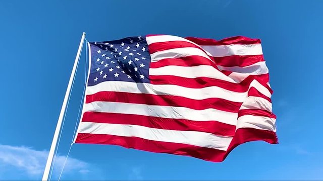 Flag of the United States of America waving in the wind against a blue sky.
