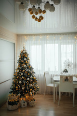 a beautiful Christmas tree with gold and white decor and gifts under the Christmas tree in a light beige interior of the apartment, with a white table and white chairs in a gold decor against a backg