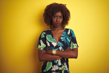 Young african afro woman wearing summer floral dress over isolated yellow background skeptic and nervous, disapproving expression on face with crossed arms. Negative person.