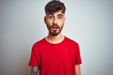 Young man with tattoo wearing red t-shirt standing over isolated white background afraid and shocked with surprise expression, fear and excited face.