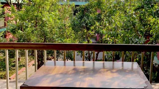 Wooden table placed in a balcony with green trees and plants in thr foreground