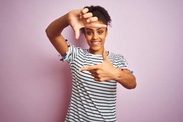 African american woman wearing navy striped t-shirt standing over isolated pink background smiling making frame with hands and fingers with happy face. Creativity and photography concept.