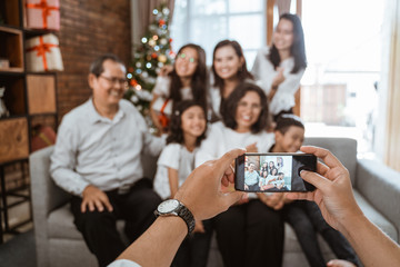 family taking photo together using phone on christmas day celebration sitting on a couch at home
