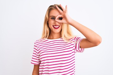 Young beautiful woman wearing pink striped t-shirt standing over isolated white background doing ok gesture with hand smiling, eye looking through fingers with happy face.