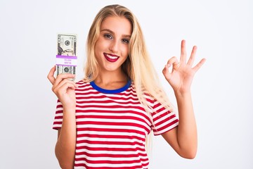 Obraz premium Beautiful woman wearing red striped t-shirt holding dollars over isolated white background doing ok sign with fingers, excellent symbol