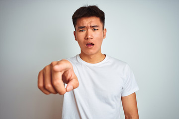 Young asian chinese man wearing t-shirt standing over isolated white background pointing displeased and frustrated to the camera, angry and furious with you