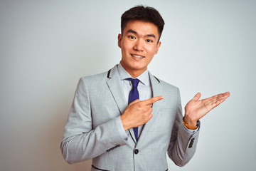 Asian chinese businessman wearing suit and tie standing over isolated white background amazed and smiling to the camera while presenting with hand and pointing with finger.