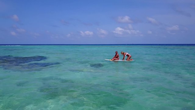 Young women trying to paddle surfboard on shallow lagoon with clear crystal water near shore of exotic island in Bermuda