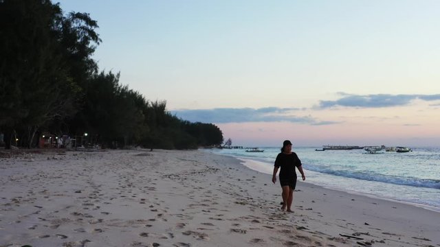 Tourist girl walking barefoot on white clean beach watching  around amazing seascape at sunset colorful sky in Thailand