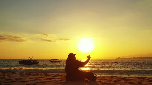 Girl passionate about photography making photos at beautiful sunset sitting on exotic beach washed by sea waves in Indonesia