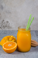 Fototapeta na wymiar Mango smoothie with orange in a jar and with tubes stands on a gray concrete background. Clean and healthy food for vegetarians. Healthy diet.