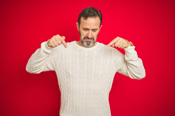 Handsome middle age senior man with grey hair over isolated red background Pointing down looking sad and upset, indicating direction with fingers, unhappy and depressed.