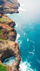 Vertical shot of the rocky cliffs by the beautiful calm blue ocean captured in Kauai, Hawaii