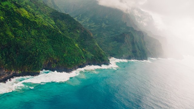 High angle shot of the foggy cliffs over the calm blue ocean captured in Kauai, Hawaii
