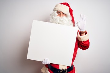 Middle age man wearing Santa Claus costume holding banner over isolated white background doing ok sign with fingers, excellent symbol