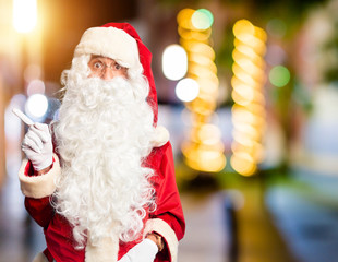 Middle age handsome man wearing Santa Claus costume and beard standing Surprised pointing with finger to the side, open mouth amazed expression.